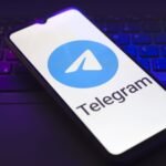 The Telegram logo appears on the screen of a smartphone that rests on top of a laptop keyboard
